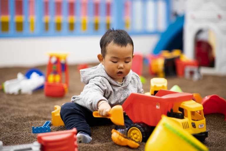 Boy in sandpit playing sitting with clean baby toys for germ-free play.