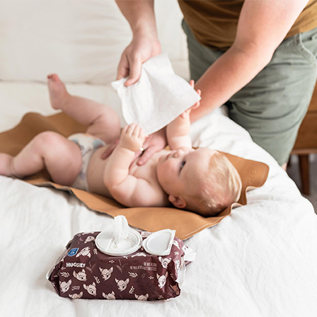 Baby pulling Huggies® Calm™ Baby Wipes form a person's hand who trying to wipe