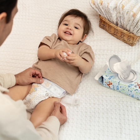 Father changing child’s diaper with Huggies® Natural Care® Cucumber, Aloe & Vitamin E Baby Wipes in the background