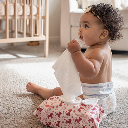 Young baby sitting upright while holding a singular Huggies® Nourish™ Wipe