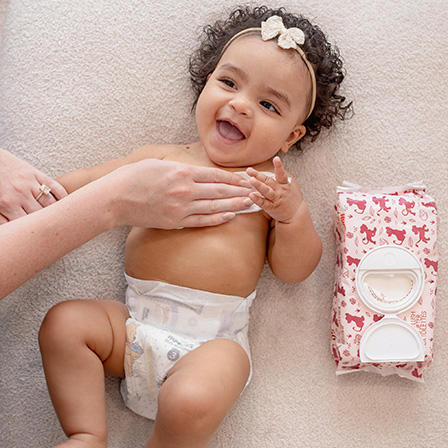 A baby smiling after a diaper change while a parent uses Huggies® Nourish™ Baby Wipes on it’s belly